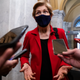 Senator Elizabeth Warren stands with phones outstretched toward her as she gives an interview at the U.S. Capitol.